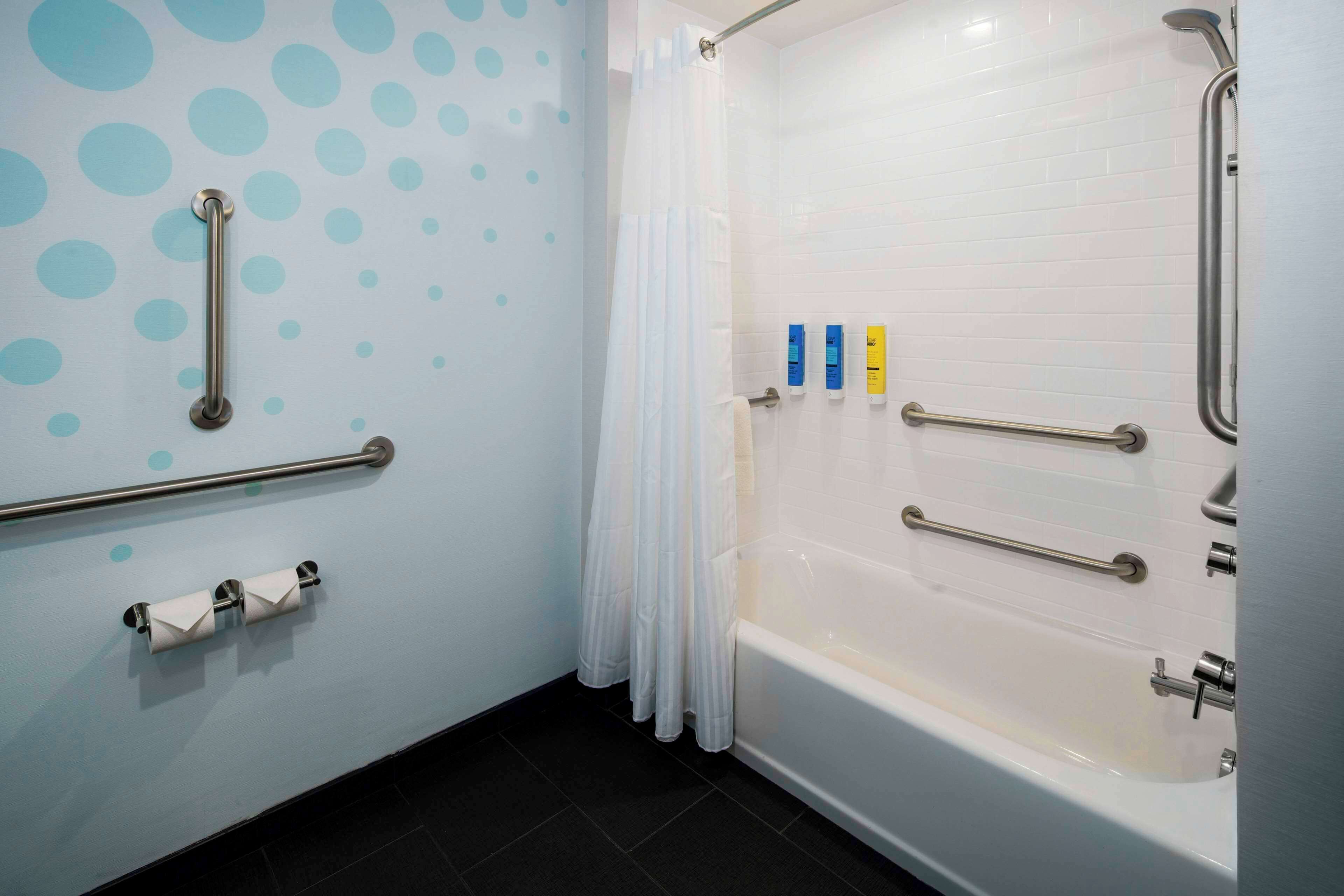 Une salle de bain équipée d’une baignoire, de barres d’appui, d’un porte-rouleau de papier toilette et d’un rideau de douche.