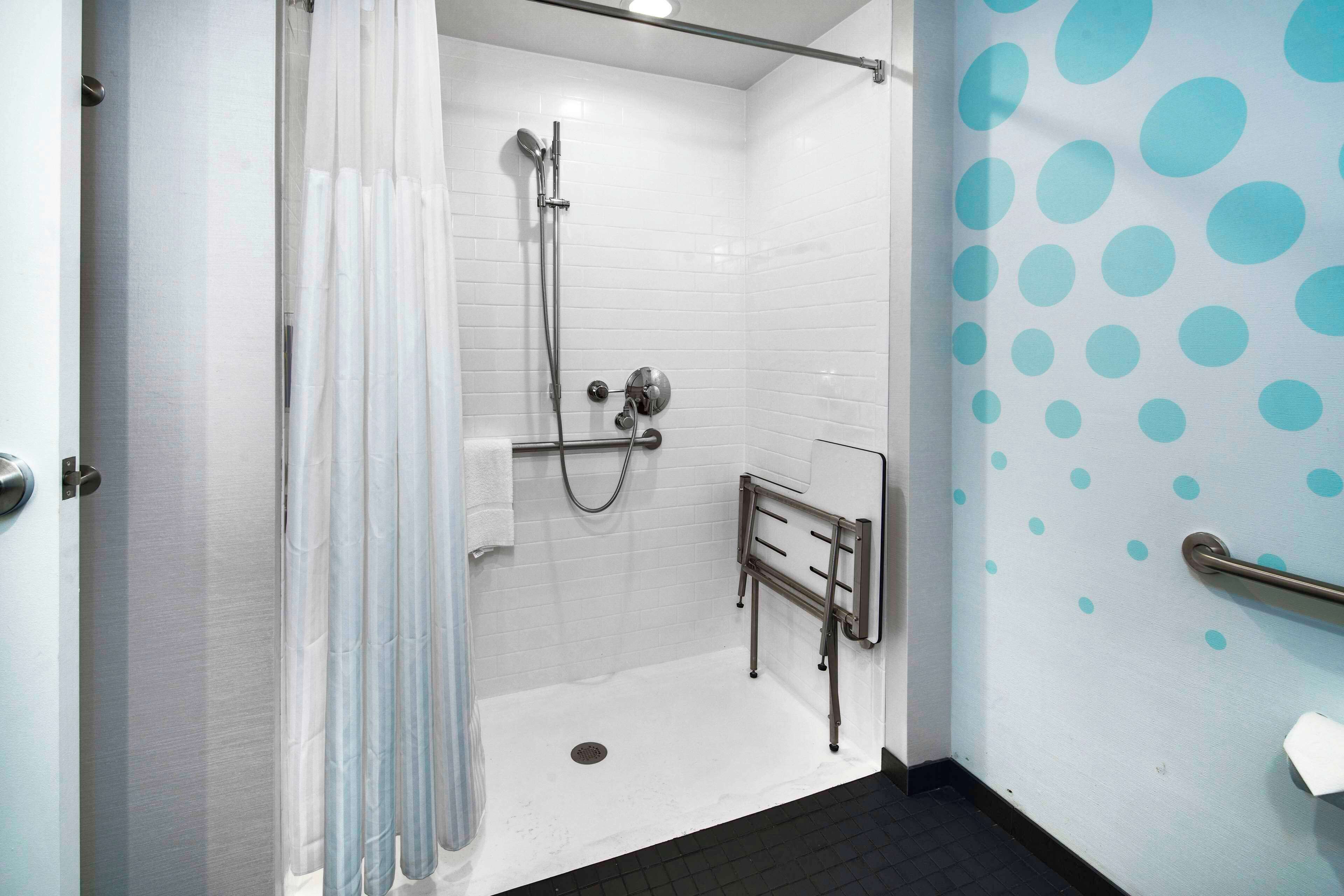 A shower area with a glass door, a handrail, and a tiled wall with blue polka dots.