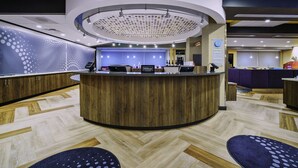 A hotel reception area with a curved wooden counter, a modern ceiling design, and a herringbone-patterned floor. - Tru By Hilton Goodyear Phoenix West, AZ (Goodyear)