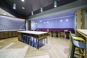 A modern bar area with a wooden bar counter, blue stools, and a purple seating area.