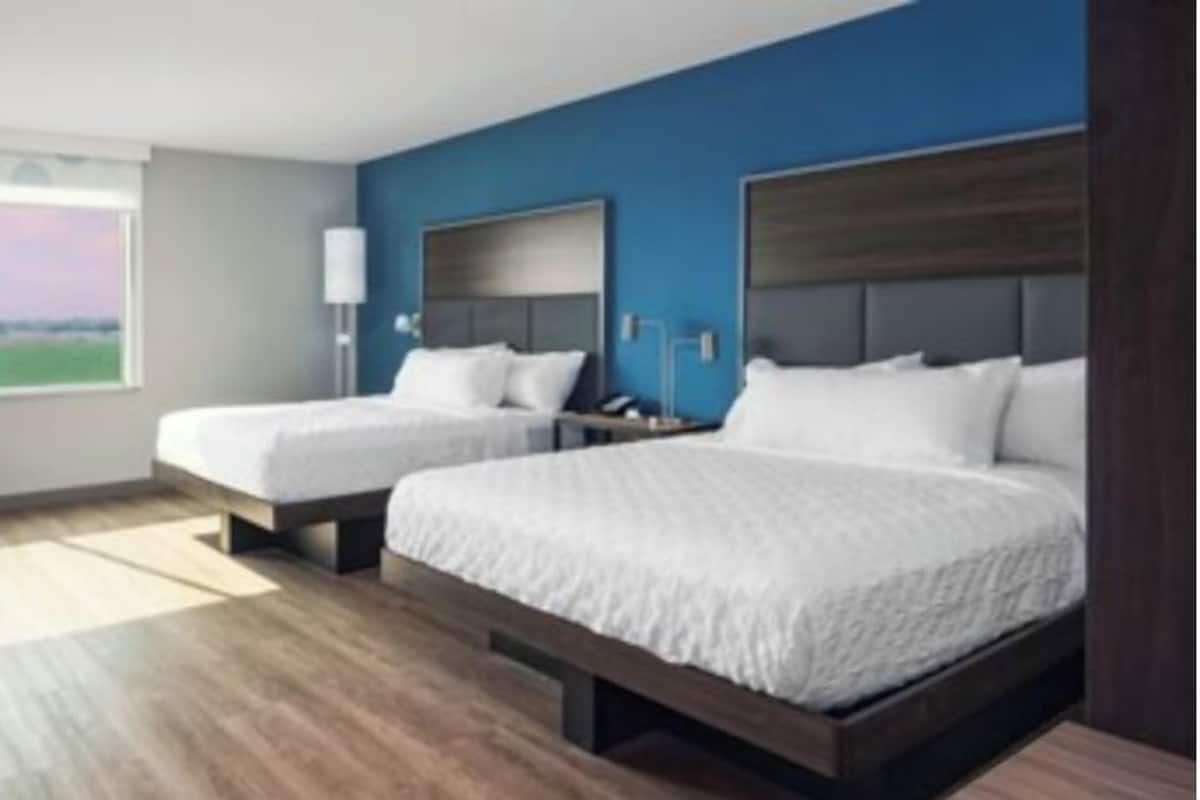 A hotel room with two beds, a large window, and a view of the outdoors.