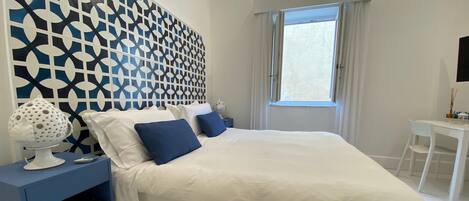 A modern bedroom with a large bed, a blue bedside table, a decorative lamp, and a geometric-patterned wall.