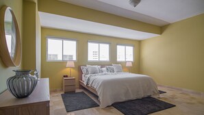 Un dormitorio con cama, mesitas de noche, un espejo y un florero sobre un tocador.