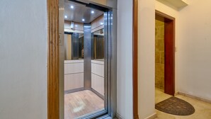 Un ascensor con puerta de vidrio transparente, una puerta de madera a su lado y suelo de baldosas.
