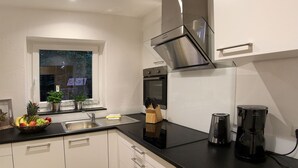 Et moderne køkken med hvide skabe, en sort bordplade, rustfrie stålgrejs og et vindue med udsigt.