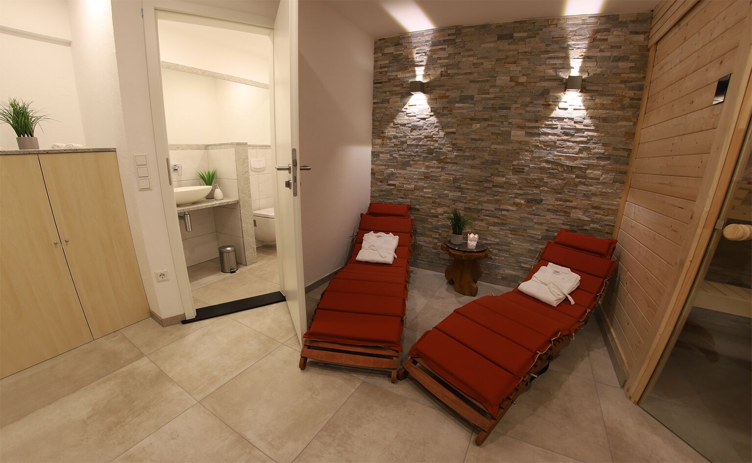Un cuarto de spa con dos camillas de masaje rojas, una pared de piedra y una pequeña mesa con una planta.