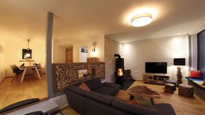 En moderne stue med en stenvæg, en sofa, et spiseområde med bord og stole, samt et fjernsyn.
