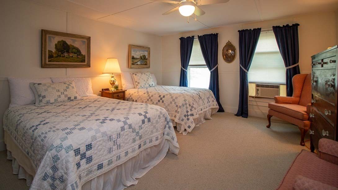 Een slaapkamer met twee bedden, een dressoir, een stoel en een plafondventilator.