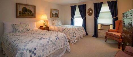 Een slaapkamer met twee bedden, een dressoir, een stoel en een plafondventilator.