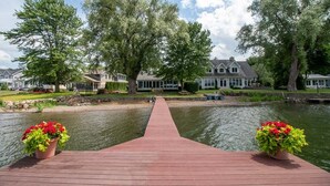 A wooden dock leading to a calm lake with houses in the background.