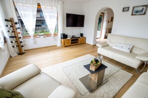 Ein modernes Wohnzimmer mit einem weißen Sofa, einem Glastisch und einem flachbildfernseher an der Wand.