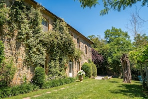 A stone building with a garden, a pathway, and a large tree.