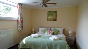 A bedroom with a bed, two bedside tables, a ceiling fan, a radiator, and a window with curtains. - Hiša Kramer - Apartment Borjana (Kobarid)