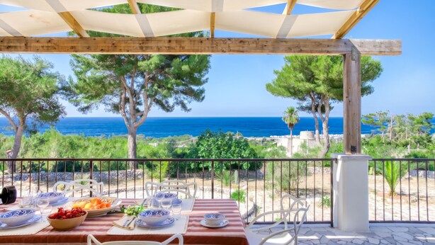 A terrace with a table set for dining, overlooking a coastal landscape with trees and the sea. - Sea view pool villa w/ garden, 2km from sand (Torre Pali)