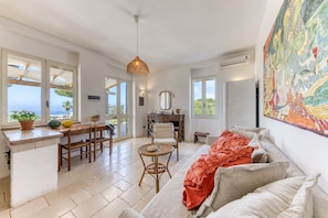 A spacious living area with a sofa, dining table, chairs, and a kitchen area with a view of the sea.