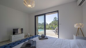 Une chambre avec un grand lit, un téléviseur posé sur une commode et une vue sur une piscine et un espace de détente extérieur.