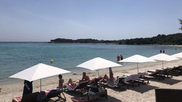 Une plage avec des chaises longues et des parasols, une mer calme et une île qui se dessine à l’horizon.