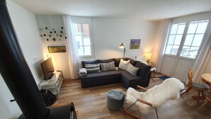 A modern living room with a sectional sofa, a white fluffy rug, a rocking chair, a fireplace, and a large window.