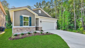 A modern two-story house with a stone foundation, a garage, and a well-maintained lawn. - COZY 4 BEDROOM RANCH NEAR JAX (Jacksonville)