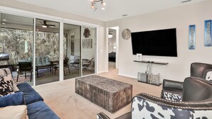 A spacious living room with a large flat-screen TV, a ceiling fan, and a sliding glass door leading to an outdoor patio. - COZY 4 BEDROOM RANCH NEAR JAX (Jacksonville)