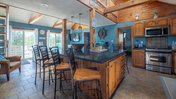 A spacious kitchen with wooden cabinets, a large island, and a dining area with chairs. - The Swan Shack - 4x4 Carova Beach, Pool, Hot Tub, Theater, Pets OK, Private Setting (Carova Beach)