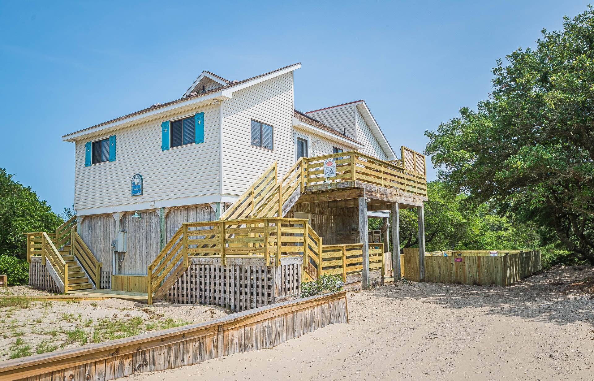 Ein zweistöckiges Strandhaus mit einer Holzterrasse und Treppen zu einer überdachten Veranda.