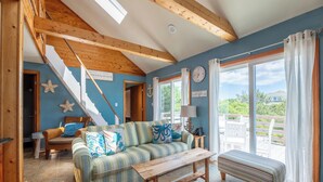 A living room with a sofa, a wooden bench, a staircase, and a view of the outdoors. - The Swan Shack - 4x4 Carova Beach, Pool, Hot Tub, Theater, Pets OK, Private Setting (Carova Beach)