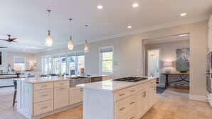 A spacious kitchen with a large island, pendant lighting, and a view of the outdoors through large windows.