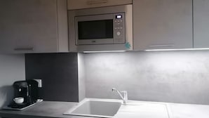 A modern kitchen with a built-in microwave, a coffee maker, and a stainless steel sink. - Beach Front Apartment (Leucate)