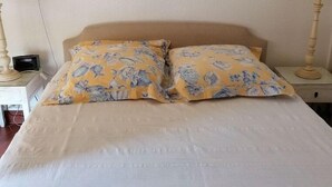 A bed with a floral duvet, two bedside tables with lamps, and two framed pictures on the wall. - Beach Front Apartment (Leucate)