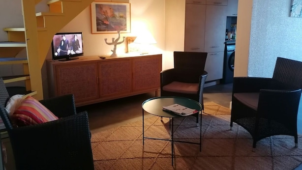 A living room with a sofa, two armchairs, a coffee table, a TV, a bookshelf, and a staircase. - Beach Front Apartment (Leucate)