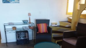 A living room with a sofa, a small table, a rug, a painting, and a staircase. - Beach Front Apartment (Leucate)