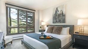 Une chambre avec une grande fenêtre, un lit sur lequel se trouve un plateau avec des articles pour le petit-déjeuner, un tableau accroché au mur et une table de chevet avec une lampe.