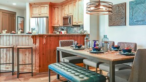 Une cuisine moderne avec des meubles en bois, un réfrigérateur en acier inoxydable et un coin repas comprenant une banquette et des chaises.