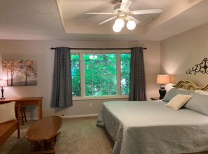 Ein Schlafzimmer mit einem Bett, einem Schreibtisch, einem Stuhl, einem Fenster mit Vorhängen, einem Deckenventilator und einer Wandlampe.