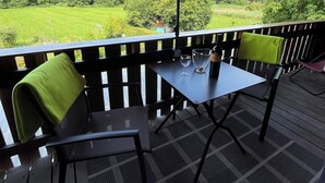 Eine Terrasse im Freien mit Tisch und Stühlen, einem roten Sonnenschirm und Blick auf eine grüne Landschaft.