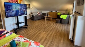 Ein geräumiger Wohnbereich mit Flachbildfernseher, einer Couch, einem Couchtisch und Holzboden.
