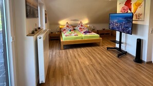 Ein modernes Schlafzimmer mit Holzboden, einem Bett mit farbenfroher Bettwäsche, einem Fernseher und Kunstwerken an den Wänden.