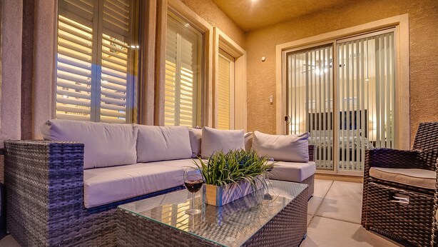 Un espace extérieur accueillant avec un canapé en osier, une table basse en verre et une plante en pot.