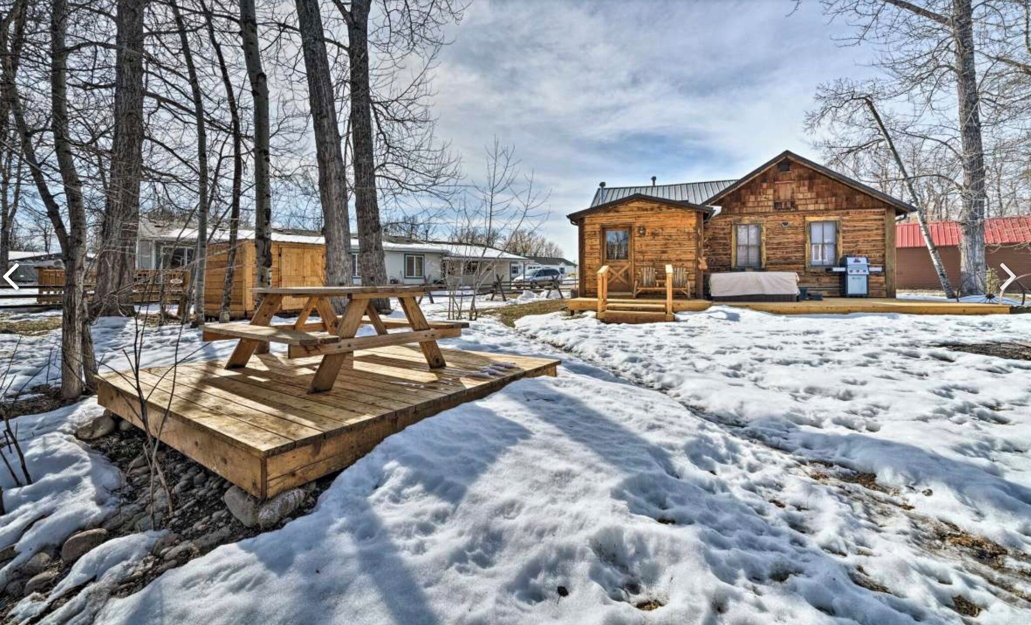 A wooden cabin with a deck, surrounded by trees and snow.