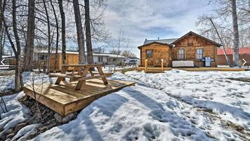 A wooden cabin with a deck, surrounded by trees and snow.