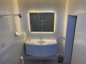 Uma casa de banho moderna com um lavatório branco, um espelho e um porta-toalhas.