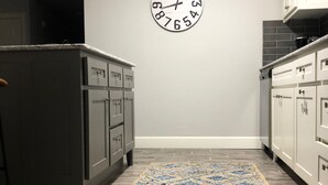 Eine Küche mit grauen Schränken, einem gemusterten Teppich und einer Wanduhr.