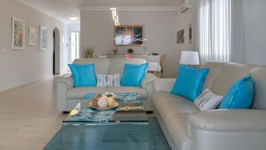 Un salon spacieux avec un canapé beige, une table basse agrémentée d’objets décoratifs et un lustre moderne.