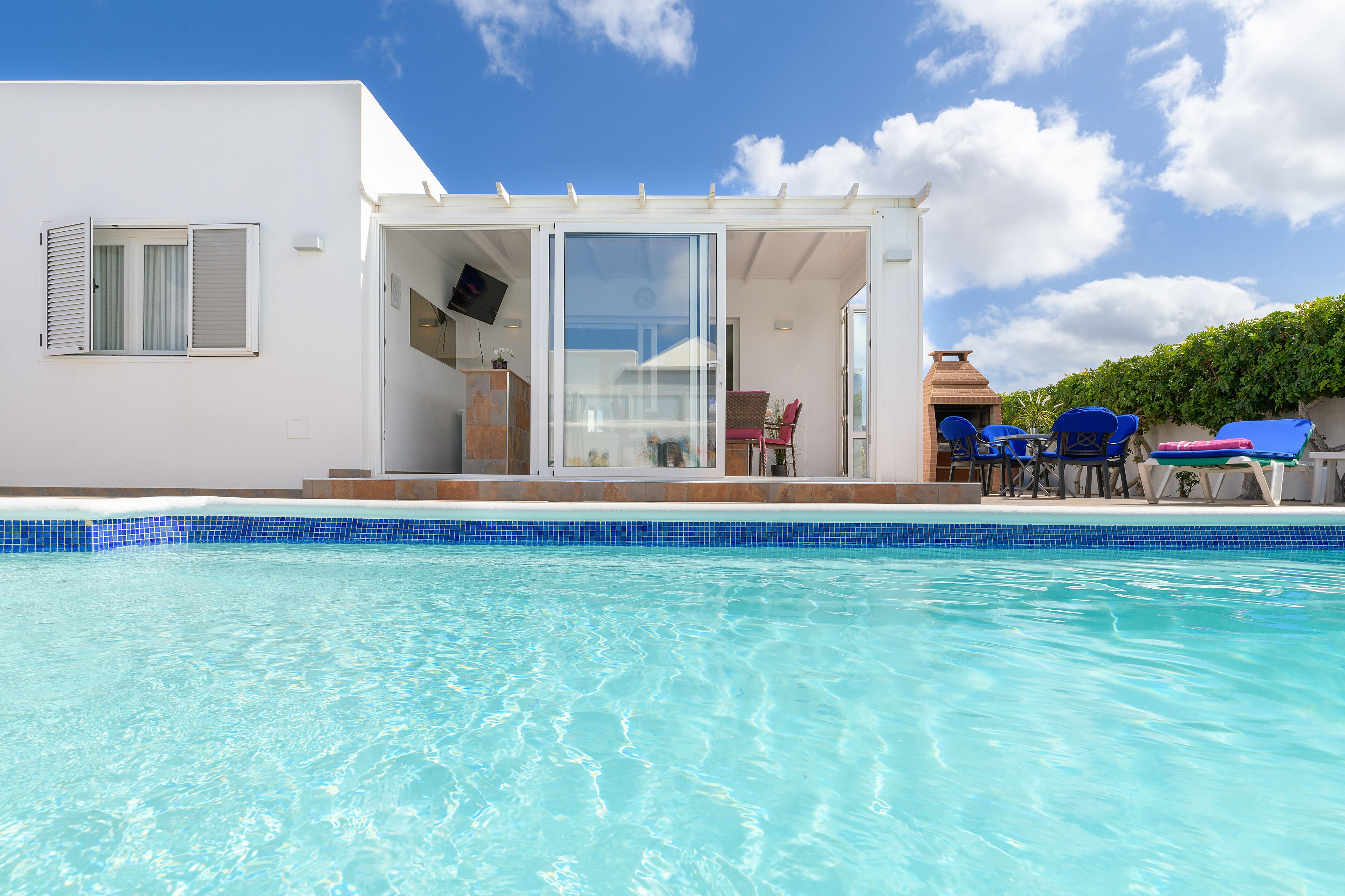 Une maison moderne dotée d’une piscine, d’une terrasse avec des chaises et d’un téléviseur fixé au mur.