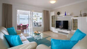 A modern living room with a glass coffee table, beige sofas with blue cushions, a flat-screen TV, and a dining area with a table and chairs. - Private villa with pool and whirlpool in a quiet location (Puerto del Carmen)