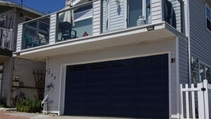 Una casa a due piani con garage, un balcone con sedie e un cielo azzurro limpido.