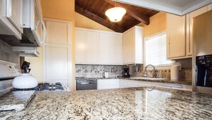 Cucina con mobili bianchi, piano di lavoro in granito, lavello in acciaio inossidabile e lampada moderna.