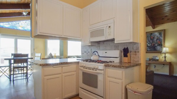 A kitchen with white cabinets, a microwave, a stove, and a trash bin.