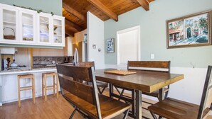 Un'area pranzo con tavolo e panche in legno, una cucina con mobili bianchi e un quadro appeso al muro.
